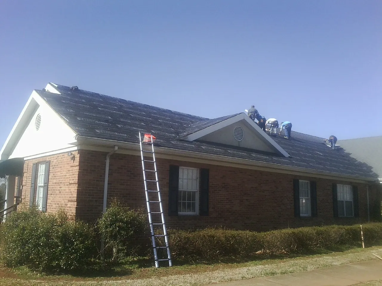 Crew tearing shingles off a brick ranch roof with a ladder set — Emergency Roof Repair work by our crew in Stockett