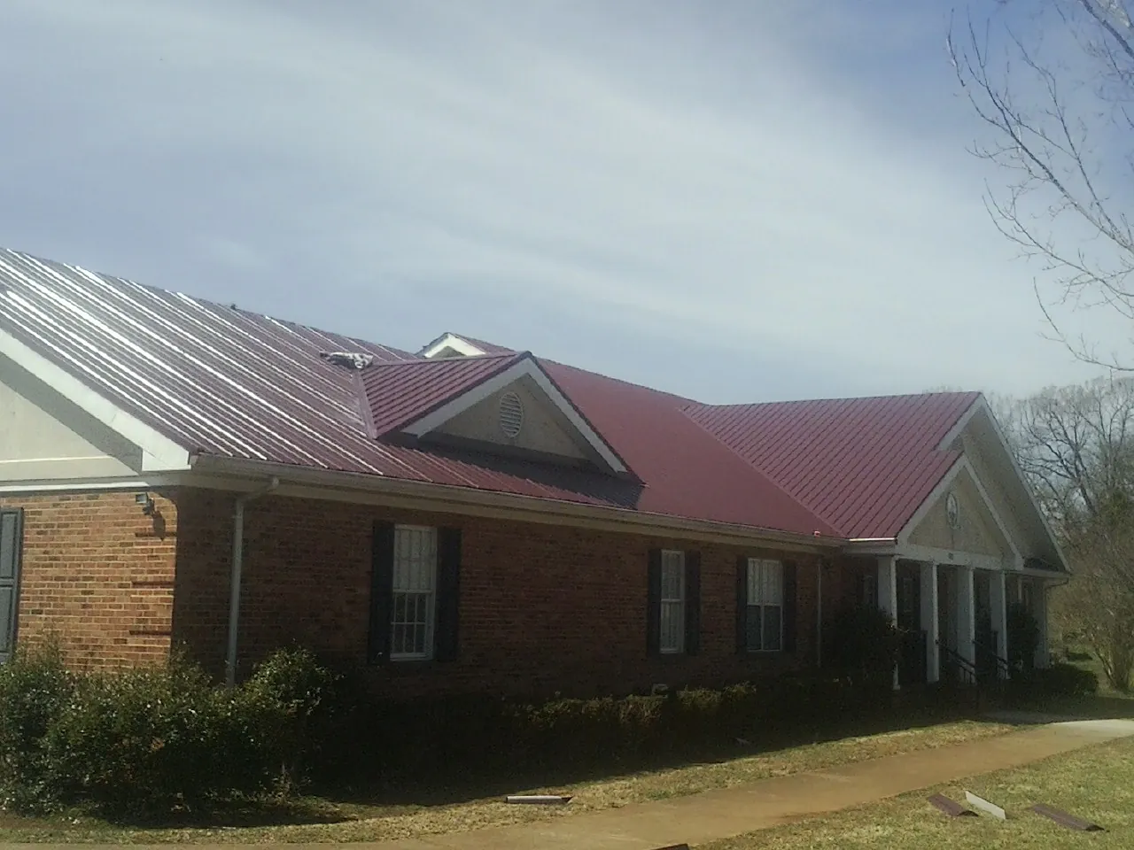 Red metal roof with gabled entries on a long brick building, from a Hail Damage Roof Repair job in Stockett