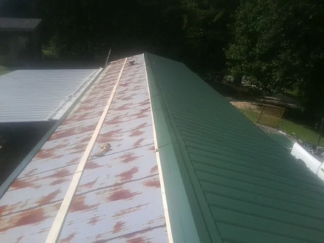 Old rusted panels beside newly installed green metal roofing — Wind Damage Roof Repair by Roofing Brothers in Stockett
