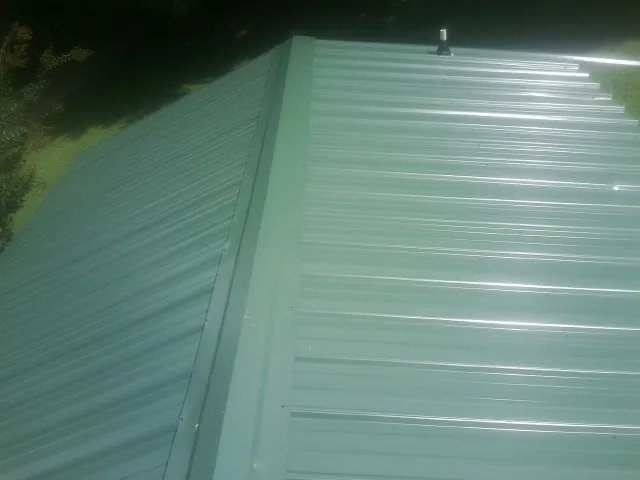 New green metal panels meeting at the ridge of a roof — Flat Roof Repair work by our crew in Stockett