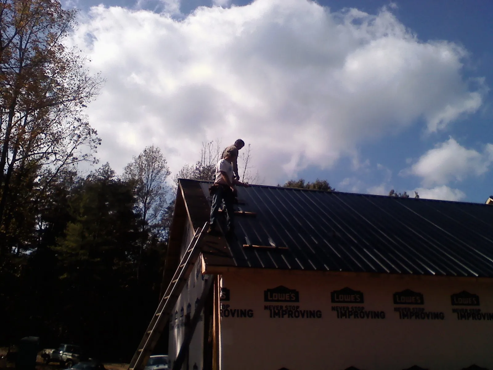 Roofer fastening dark metal panels high against a cloudy sky, from a Roof Inspection job in Stockett