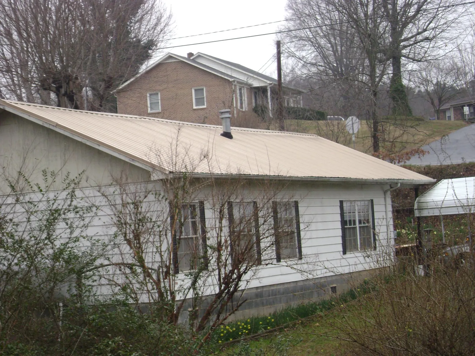 Tan metal roof on a white sided house set into a hillside — Commercial Roofing by Roofing Brothers in Stockett