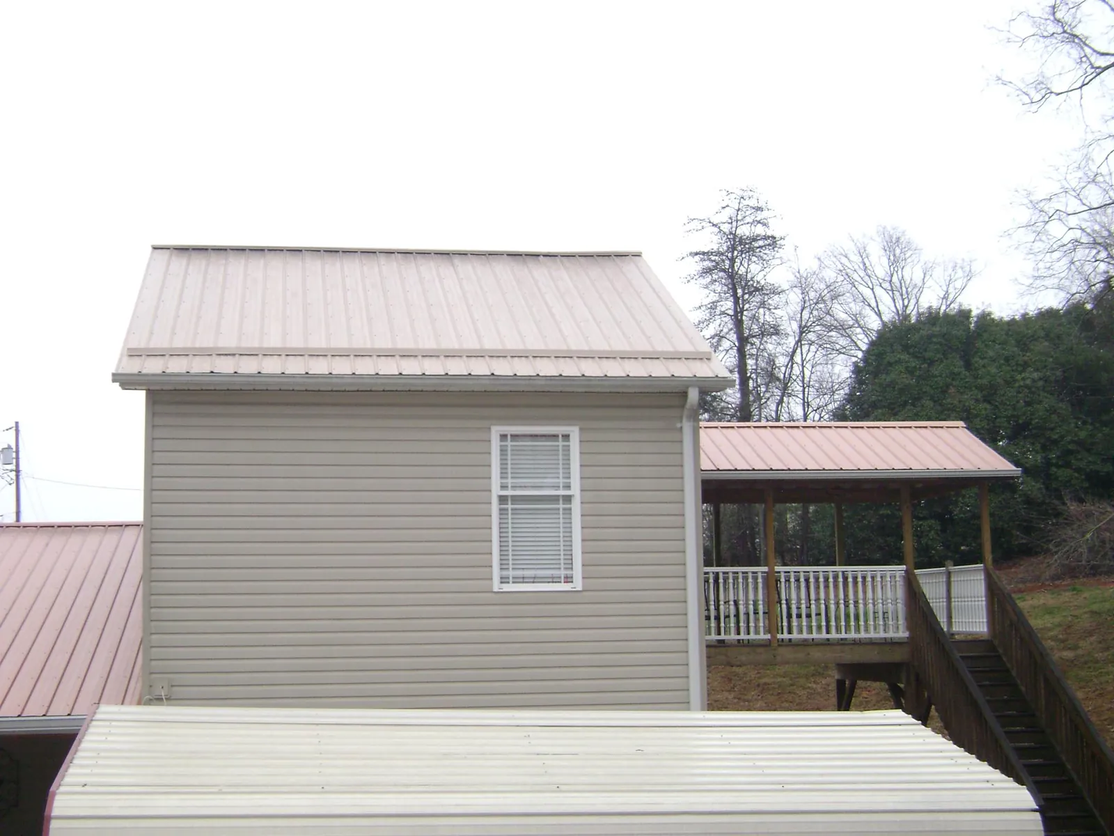 Tan metal roofs on a two story addition and attached porch, from a Roof Replacement job in Stockett